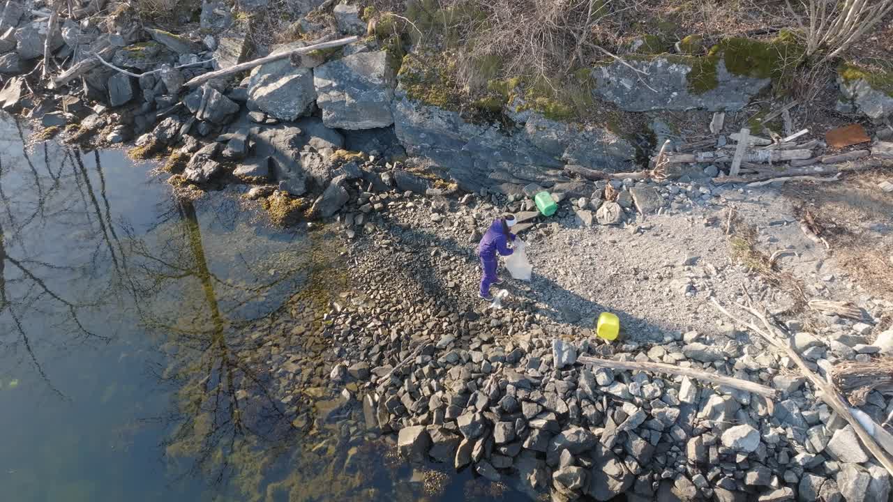 Aerial view of woman removing plastic waste from small rocky beach in Norway