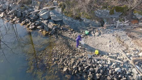 aerial view of woman removing plastic waste from small rocky beach in norway