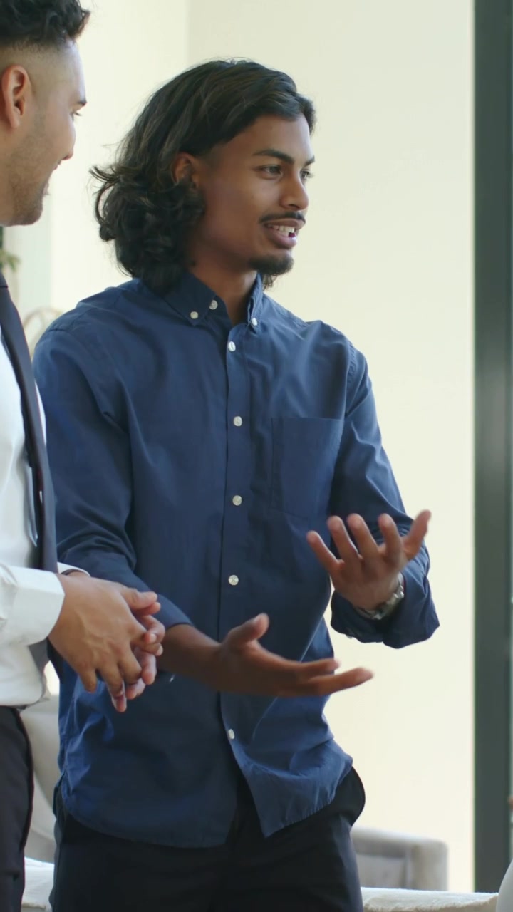 Vertical video: Starting navy-shirted man explaining, gesturing in living room near grid window