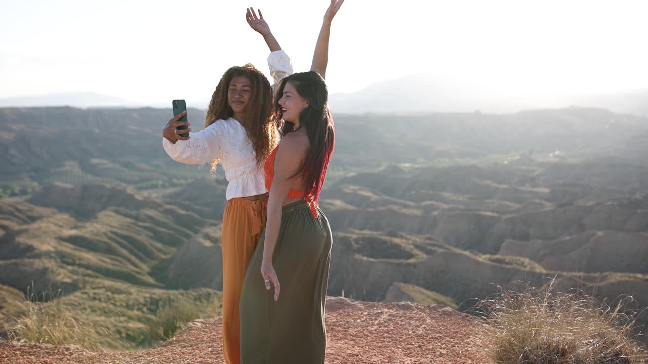 Two friends taking a selfie with a scenic desert landscape at sunset