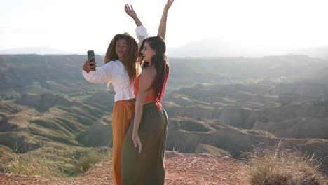 two friends taking a selfie with a scenic desert landscape at sunset