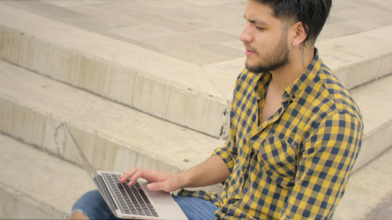 hombre guapo sentado en las escaleras usando una computadora portátil al aire libre