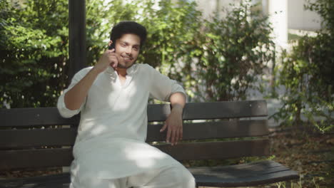 young muslim man sitting on bench, talking on his cellphone.