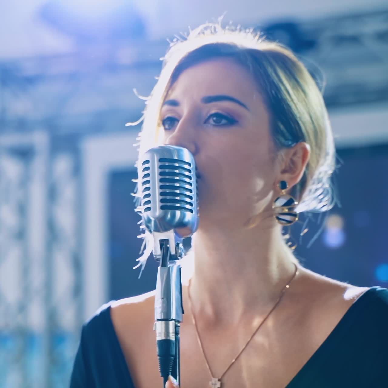 Woman singer on the stage. Beautiful girl performing a song into the microphone on the background of video on stage.
