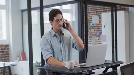 man using laptop and talking on smartphone while sitting on his desk