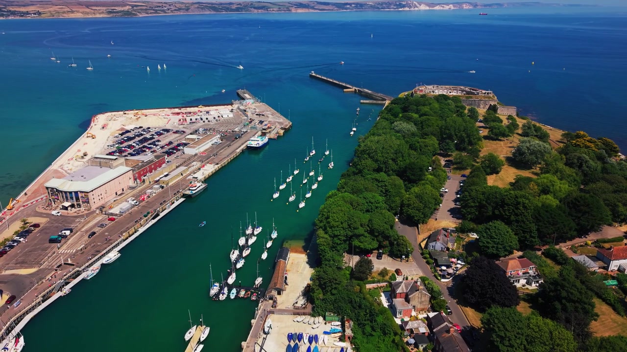 Vista drone sull'ingresso del porto di Weymouth, che mostra barche a vela ormeggiate, le mura del porto, il Forte Nothe e le acque blu della Baia di Weymouth