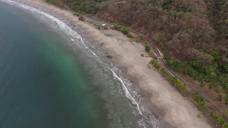 beach coastline of costa rica with soft waves hitting rocks on sandy shore, aerial flyover tilt down shot