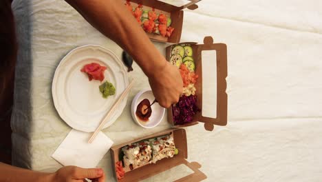 vertical video of hands pouring soy sauce on a table filled with different sushi varieties