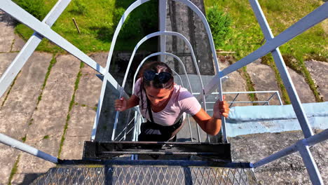 Brunette-european-woman-climbing-up-a-high-metal-ladder-in-slowmotion,-view-from-above