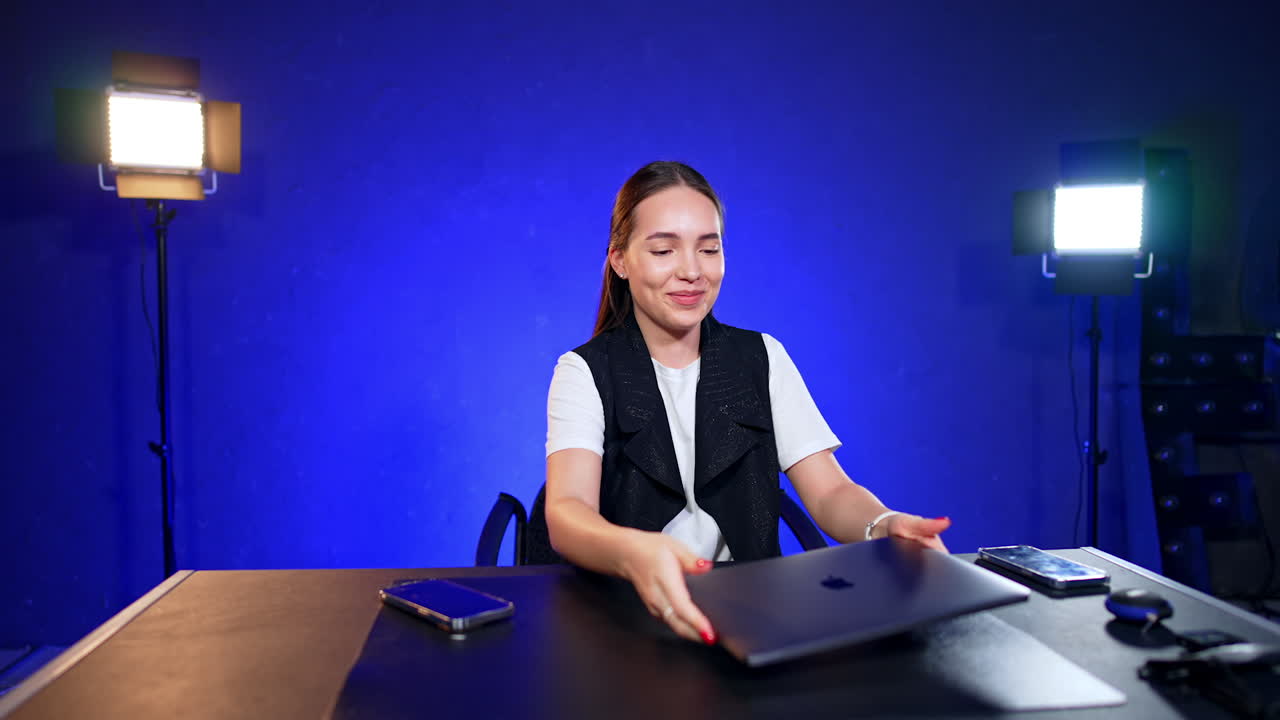 Beautiful Caucasian lady sitting at the desk and preparing gadgets. Blogger is getting ready for footage in studio.