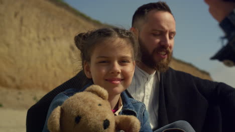 Padre-Hija-Sonriendo-Cámara-En-La-Playa-Junto-Al-Mar.-Encantadora-Familia-Disfruta-De-La-Sesión-De-Fotos.