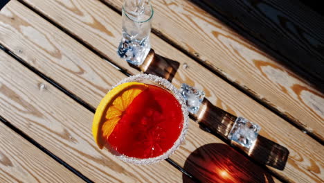 red cocktail with orange slice on a sunny wooden table