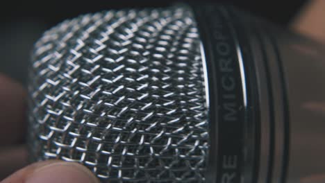 persona que sostiene un micrófono moderno en un fondo oscuro macro