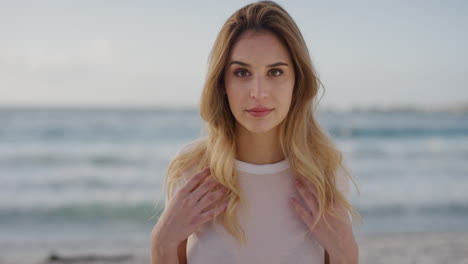 portrait of beautiful blonde woman on beach enjoying summer vacation looking at camera running hands through hair seaside background