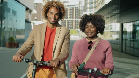 portrait of smiling african american man and woman with e-scooters in city