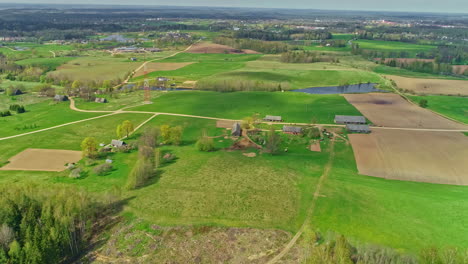 Toma-Cinemática-De-Drones-En-Movimiento-Hacia-Atrás-Que-Captura-Hermosas-Tierras-De-Cultivo-Verdes-Junto-Con-Casas-De-Campo-Durante-El-Día