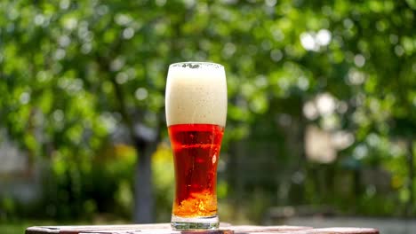 cold beer in a glass with white foam. craft beer in a glass with small bubbles inside. cool brown beverage on a table outdoors. close-up.