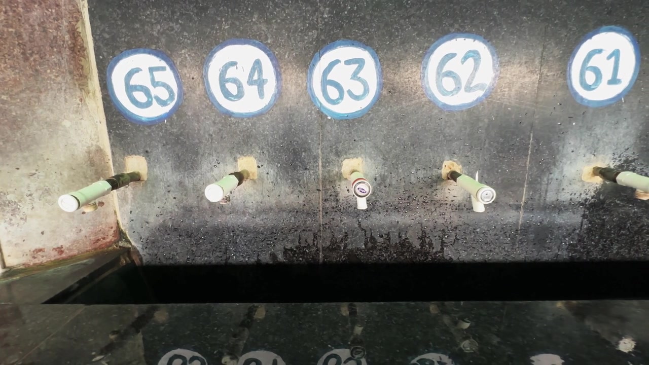 Left to right tracking shot of numbered drinking water taps with a dripping faucet in a public facility in indian railway station