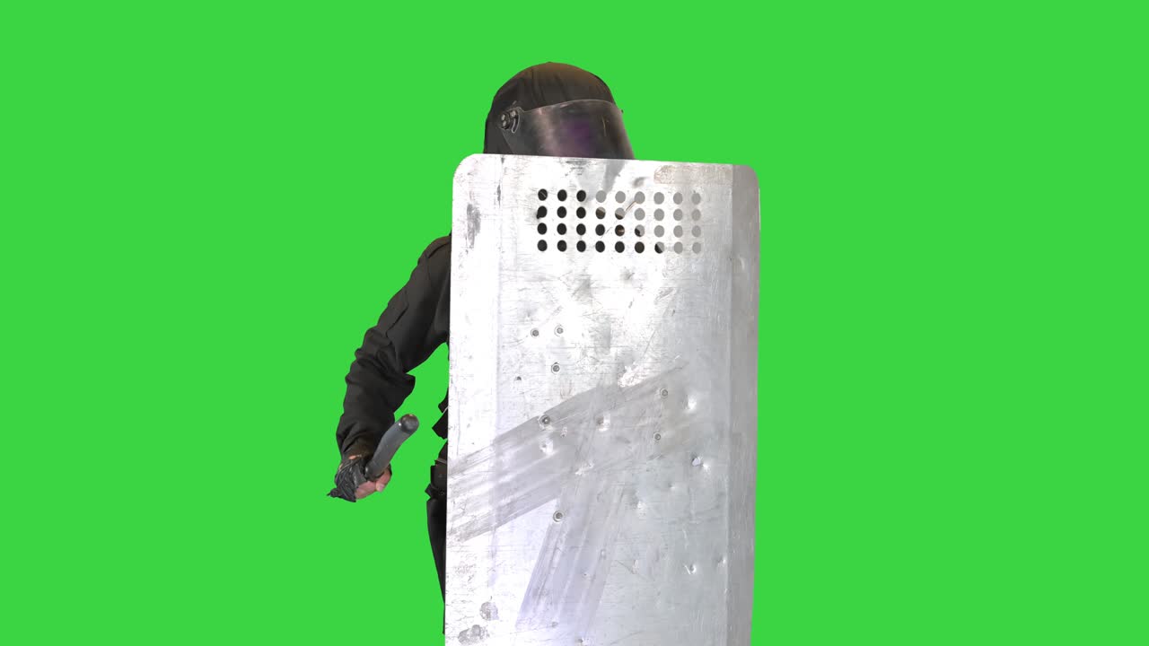 폭동 경찰이 소음을 내며 그의 폭동 방패를 녹색 스크린, 크로마 키에 지이로 때립니다.