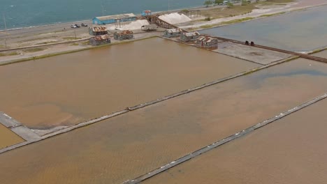 Drone-flying-over-salt-pans-with-mines-in-background,-Las-Salinas,-Bani-in-Dominican-Republic