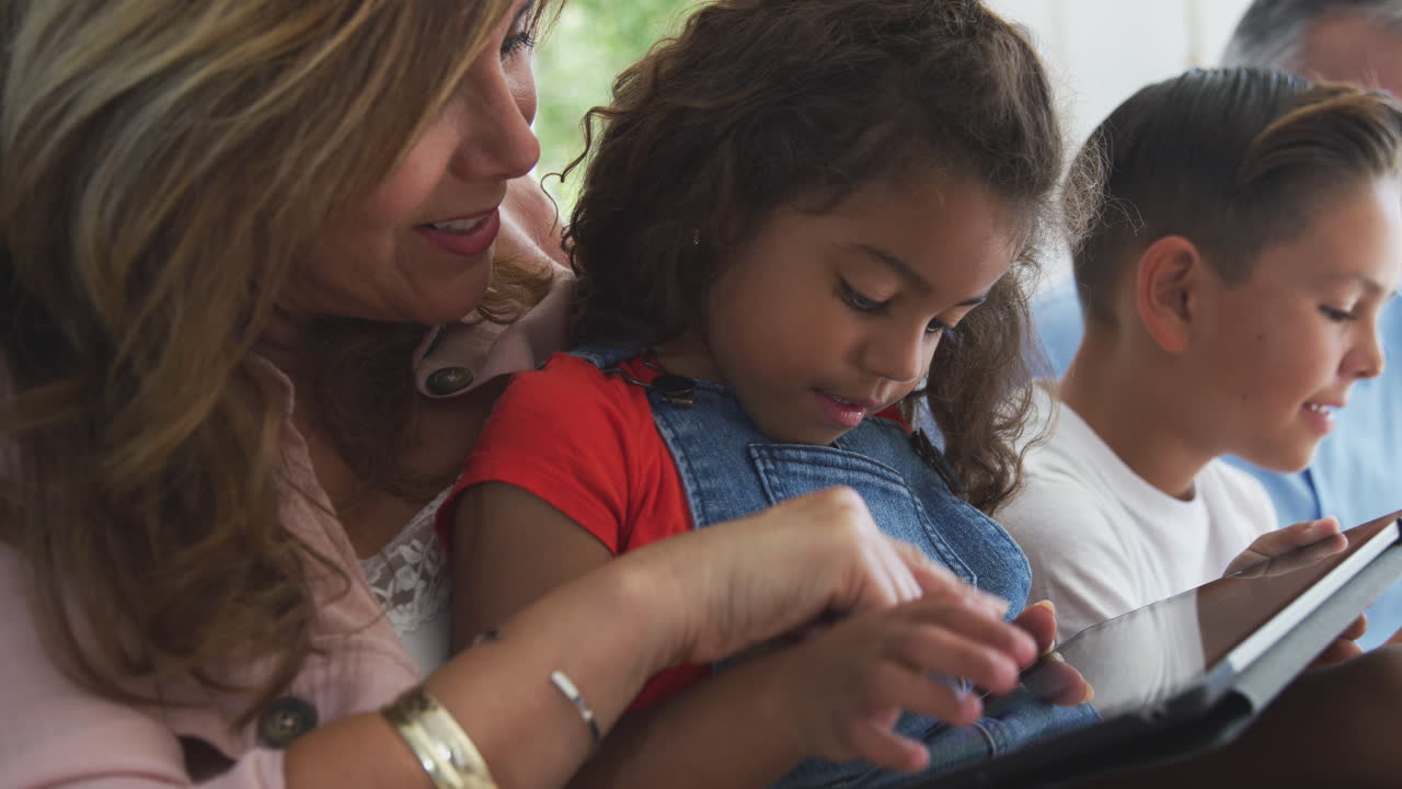 nieta con su abuela sentada en el sofá en casa usando una tableta digital