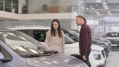 una hermosa pareja de jóvenes en la sala de exposición de automóviles eligiendo un coche nuevo para comprar.