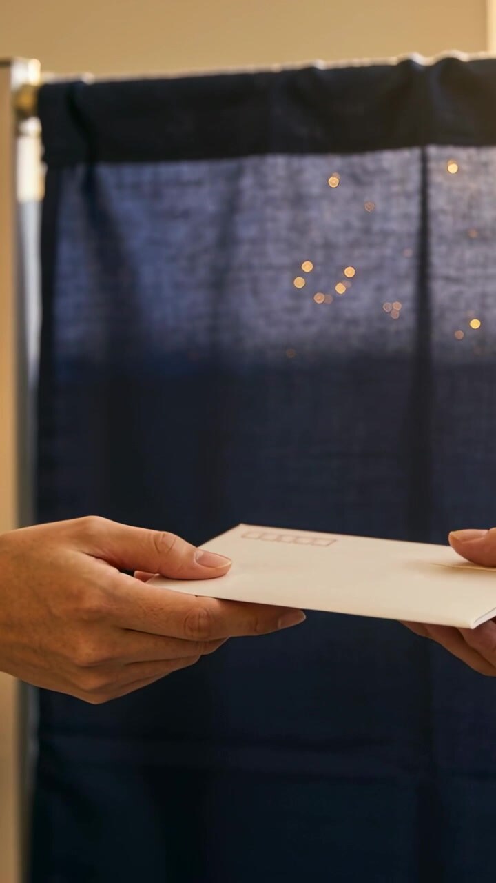 Vertical video: Left hand extending white envelope before dark-blue divider, receiver securing mail