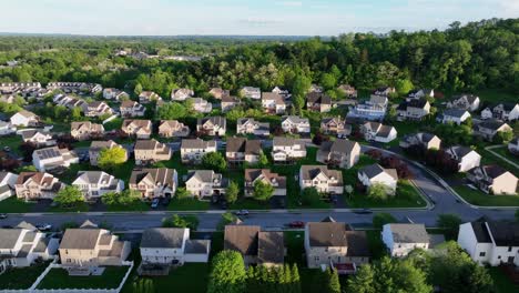 golden hour in american suburb housing area with single family houses and solar panels on roof. aerial lateral wide shot. green trees on mountains in pennsylvania state, united states. may in spring.
