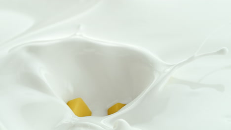 mango cubes falling into creamy milk making splashes in macro and slow motion