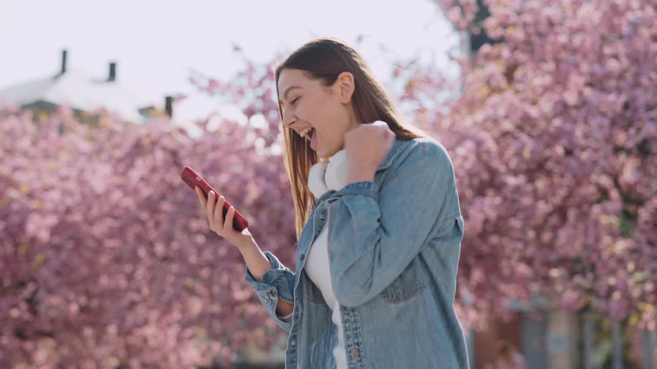 Woman using phone in a park with cherry blossoms