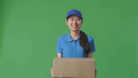 asian female courier in blue uniform smiling while delivering a carton on green screen background in the studio