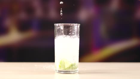 a sequence showing liquid being poured into a glass with ice and lime, set against a blurred background