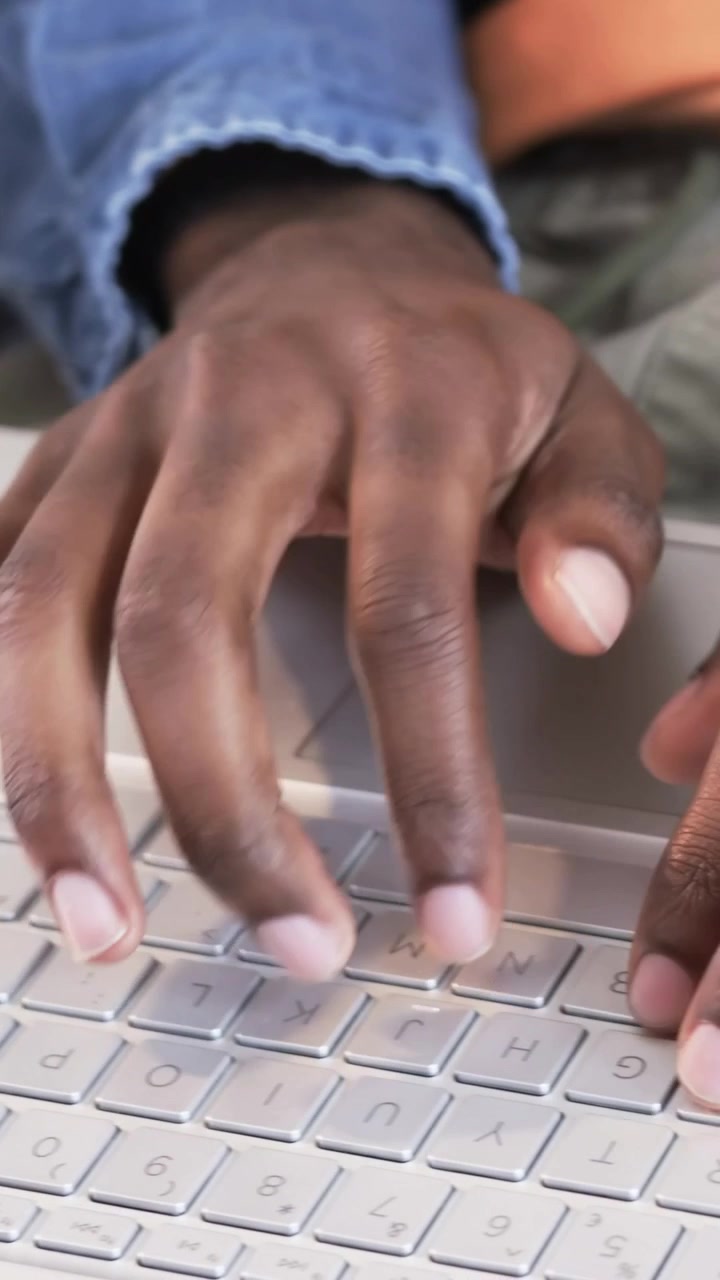 Vertical video: Camera panning to white laptop, man in denim jacket typing email on sofa, notebook