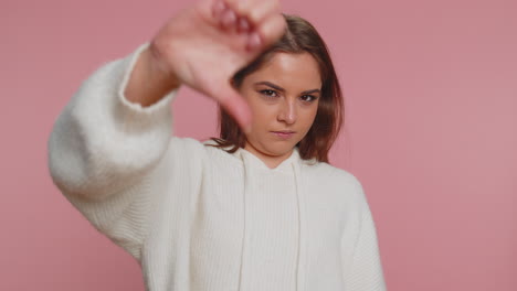 Upset-woman-in-white-sweater-showing-thumbs-down-sign-gesture,-disapproval,-dissatisfied-dislike