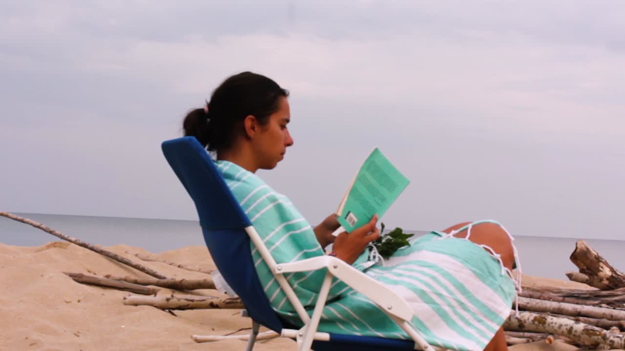Ragazza che legge un libro in spiaggia.