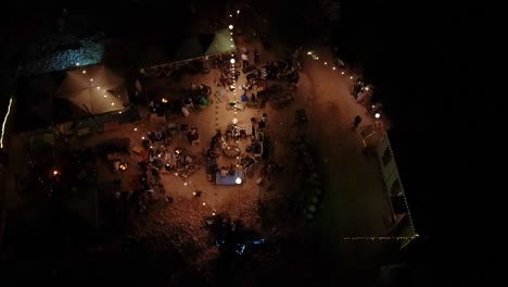 aerial drone flight over a group of people celebrating during an event at night time. orbit shot of gathering at home filled with light.