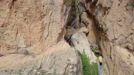 climber ascending a vertical rock wall next to a waterfall