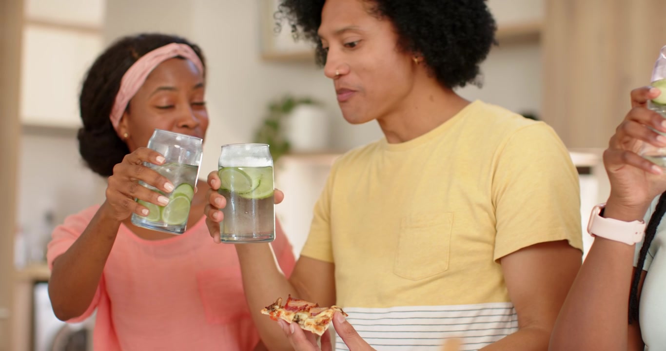 Amici afroamericani che si scambiano sguardi, alzano acqua al cetriolo e brindano con la pizza in cucina.