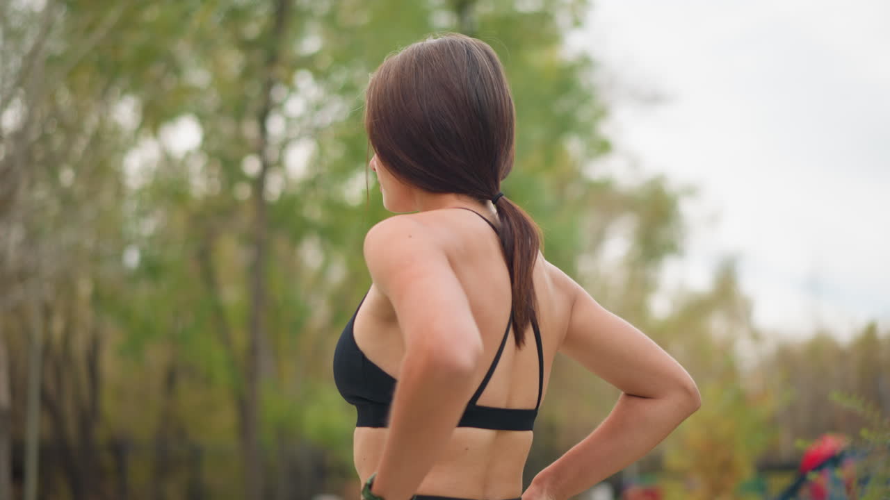 Rotation view of young athlete in black neck top placing hand on waist and breathing deeply, relaxed moment, calm expression, outdoors, fitness moment, body posture, fresh air, relaxation