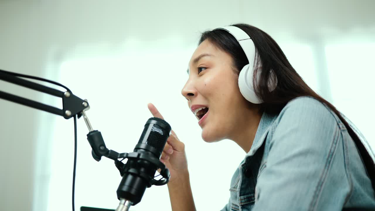 컨텐츠 제작자 여성 호스트는 헤드폰과 마이크로 노트북에서 캐스트를 스트리밍하고 방송 스튜디오에서 게스트 대화를 응원합니다.