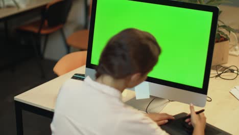 Young-woman-working-on-computer-with-green-screen-in-office.-Graphic-designer
