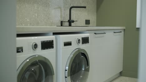 a modern laundry room with sleek white washing machines, a minimalist black faucet and sink, set against a textured beige countertop and a soothing olive wall