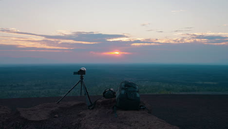 camera gear and backpack on a mountain overlooking a scenic sunset landscape