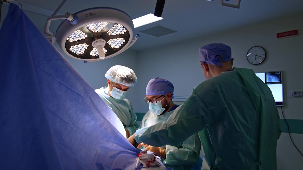 Mandligt kirurgisk team opererer patienten dækket af et blåt lagen. Akutkirurgi på et moderne hospital.