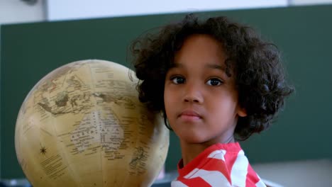 Front-view-of-African-American-schoolboy-with-globe-in-a-classroom-at-school-4k