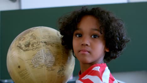 vista frontal de un escolar afroamericano con un globo en un aula de la escuela 4k