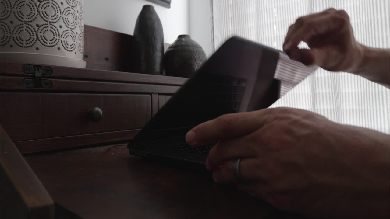 집에서 일하는 직원이 책상으로 걸어가 책상 위에 노트북 컴퓨터를 엽니다.