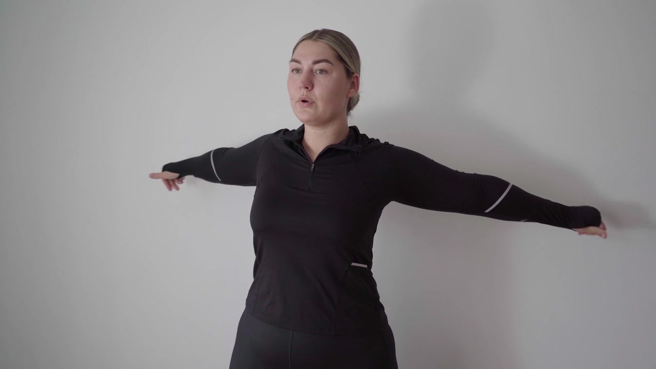 Adulto concentrado realiza círculos de brazos controlados en una habitación interior sencilla para calentar los hombros y mejorar la movilidad de la parte superior del cuerpo.