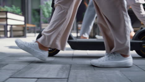 Closeup-female-legs-walking-with-electric-scooter-at-downtown-street-in-morning.