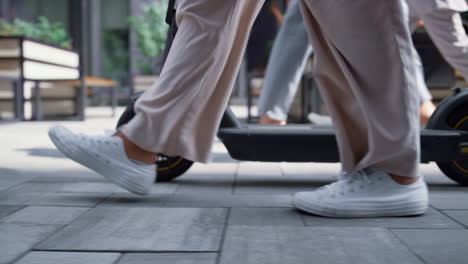 piernas femeninas en primer plano caminando con scooter eléctrico en la calle del centro de la ciudad por la mañana.